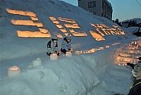 雪でできたステージにろうそくの火で浮かび上がる「３・１２防災の日」の文字＝１２日午後６時１５分、栄村の森宮野原駅前