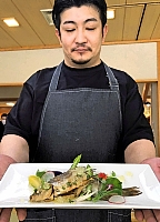 佐久市産シナノユキマスや南相木村産の野菜を使った料理を手にする鈴木さん