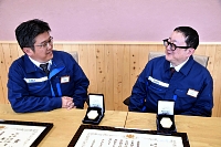 「文部科学大臣表彰」のメダルと賞状を前に語り合う平沢さん（右）と有賀さん