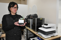 3Dプリンターなどが並ぶ工房で作った鉢植えを手にする赤羽さん