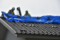 雨漏りしないよう住宅の屋根をシートで覆う作業員たち＝19日午後2時23分、大町市平