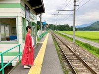 稲尾駅のホームに立つ村井美樹さん。駅のすぐ近くに水田が広がり、奥には木崎湖があります（村井さん提供）