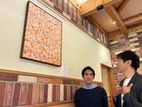 コメダ珈琲店長野駅東口公園店で展示販売している作品を前に話す佐藤社長(左)と丸山執行役員