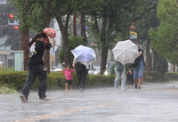 激しい雨と吹き付ける風の中、小走りする人たち＝8日午後0時50分、長野市権堂町