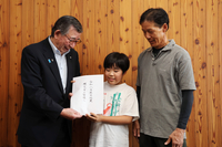 集まった寄付金を羽田健一郎町長（左）に手渡す小路さん（右）と内田さん（中央）