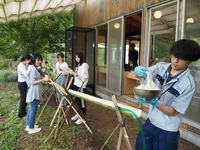 半分に切った竹を使い、流しそうめんをする大学生とタカノの若手社員（右）