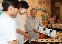 古書店での展示品を手にする金田さん（右）。展示会を前に阿南高校の生徒が見学に訪れた