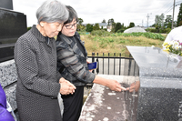 西沢船長のお墓に刻まれた「常念の山見ゆ里に眠らんと東支那海の戦に散りぬ」との言葉を読む外間さん（左）と平良館長