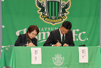 調印式で書類にサインする鎌田村長（左）と横関CEO